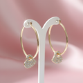 Gold hoop earrings with pavé crystal heart charm on hanging earring display with pink background